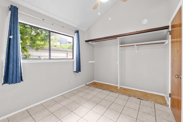 unfurnished bedroom with tile patterned floors, a closet, baseboards, a ceiling fan, and lofted ceiling