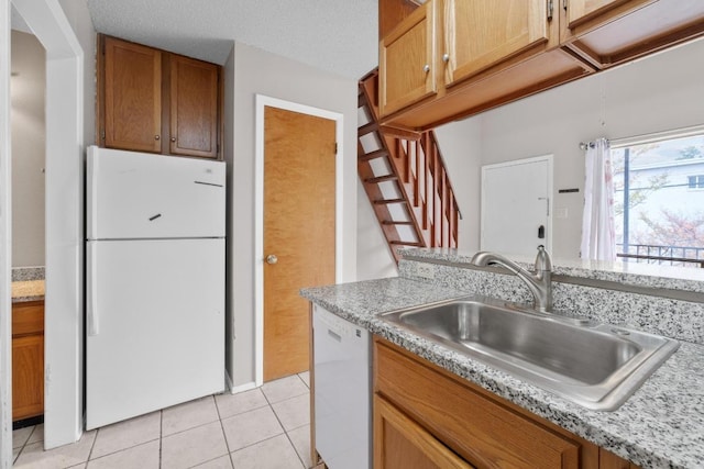 kitchen featuring white appliances, light tile patterned floors, light countertops, brown cabinets, and a sink