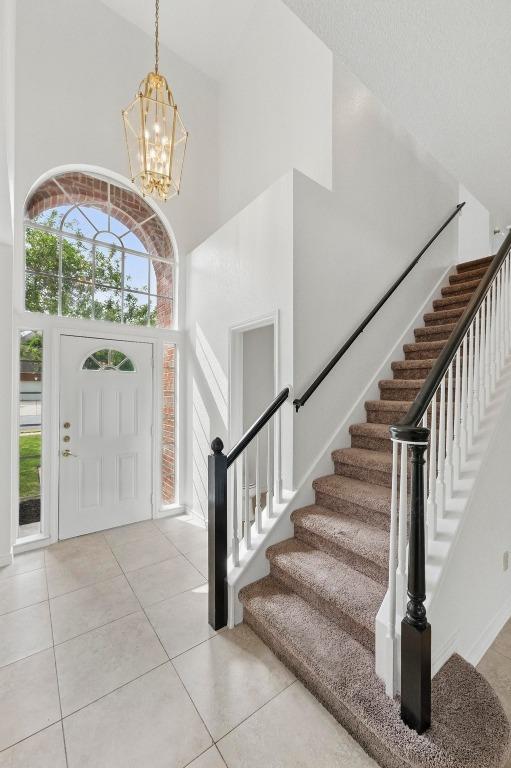 foyer entrance featuring an inviting chandelier, tile patterned flooring, stairs, and a high ceiling