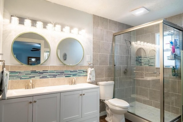 bathroom featuring double vanity, tile walls, toilet, a sink, and a stall shower