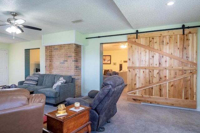living area featuring a textured ceiling, a barn door, ceiling fan, visible vents, and carpet floors