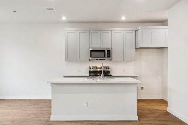 kitchen with recessed lighting, light wood-style flooring, light countertops, appliances with stainless steel finishes, and an island with sink