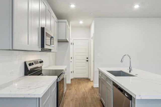 kitchen featuring a sink, appliances with stainless steel finishes, gray cabinetry, wood finished floors, and backsplash