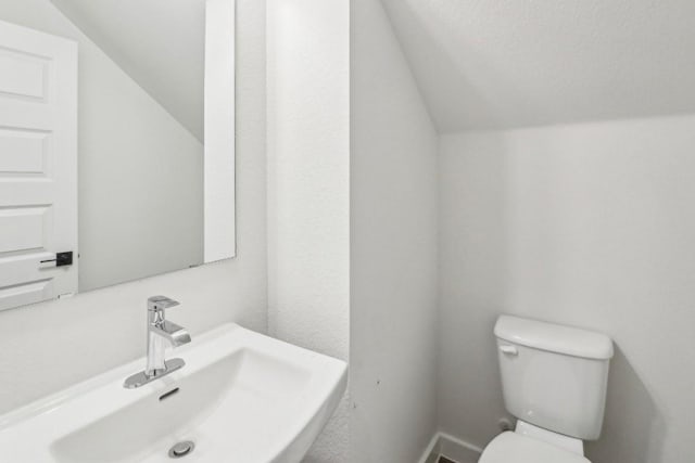 half bathroom with toilet, vaulted ceiling, and a sink