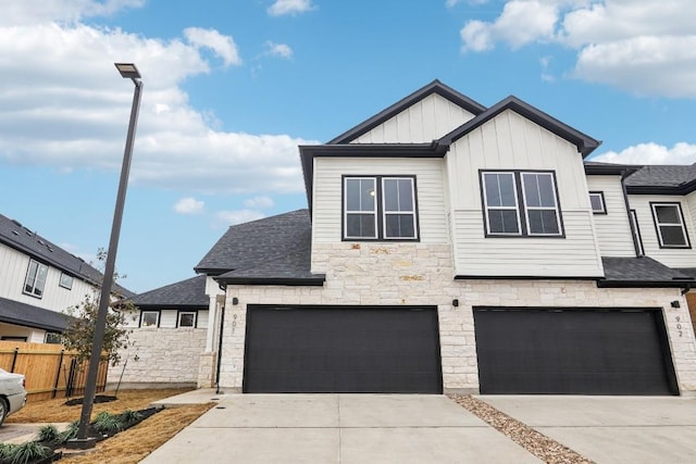 view of front facade featuring driveway, stone siding, board and batten siding, and fence