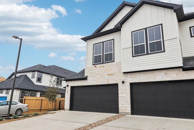 view of front of property featuring driveway, board and batten siding, stone siding, an attached garage, and fence