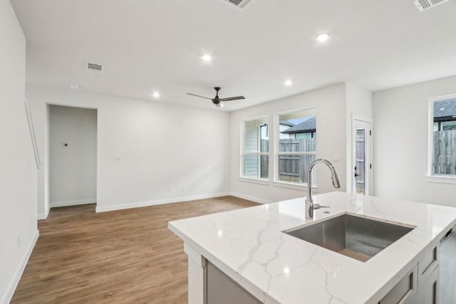 kitchen with light stone counters, a sink, visible vents, recessed lighting, and light wood finished floors