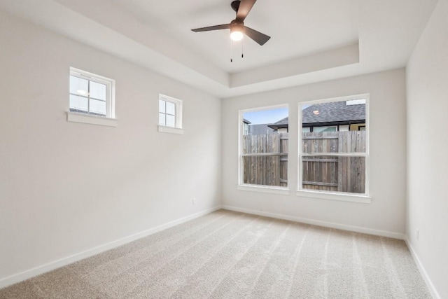 empty room featuring baseboards, a raised ceiling, ceiling fan, and light carpet