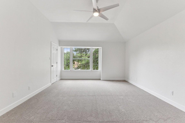 carpeted empty room with a ceiling fan, vaulted ceiling, and baseboards