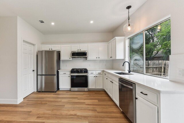 13113 Bennington Ln, Austin, TX 78753 - kitchen featuring stainless steel appliances, white cabinets, decorative backsplash, light wood finished floors, and decorative light fixtures