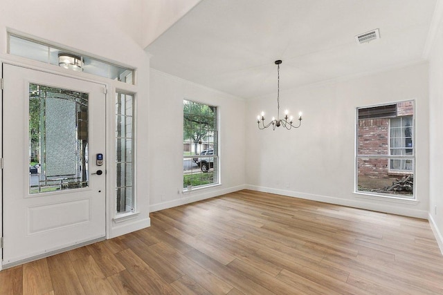 foyer with visible vents, light wood-type flooring, crown molding, and a notable chandelier