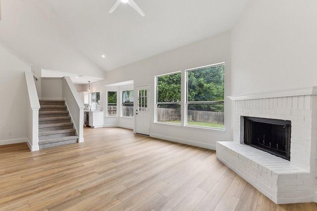 unfurnished living room with stairs, ceiling fan, a fireplace, baseboards, and light wood-type flooring