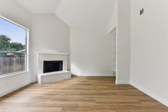 unfurnished living room featuring a brick fireplace, lofted ceiling, visible vents, baseboards, and wood finished floors