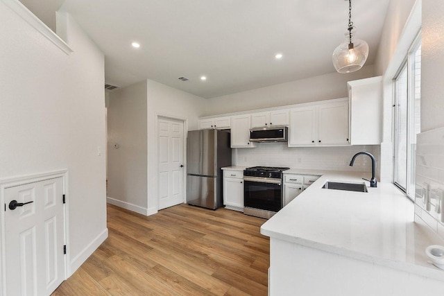 kitchen with a sink, stainless steel appliances, light wood-style flooring, backsplash, and white cabinets