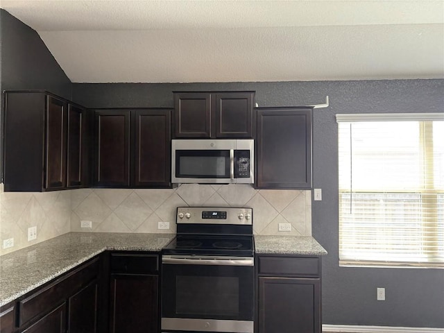 kitchen with light stone counters, vaulted ceiling, stainless steel appliances, and decorative backsplash