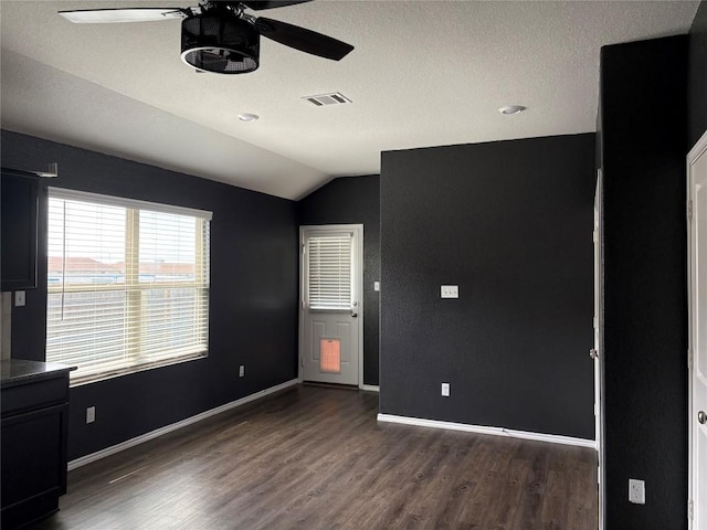 unfurnished room with vaulted ceiling, ceiling fan, baseboards, visible vents, and dark wood-type flooring