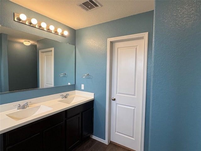 full bathroom featuring wood finished floors, a textured wall, visible vents, and a sink