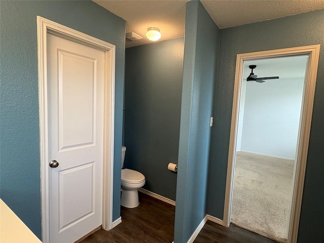 bathroom with a textured wall, baseboards, toilet, wood finished floors, and a ceiling fan