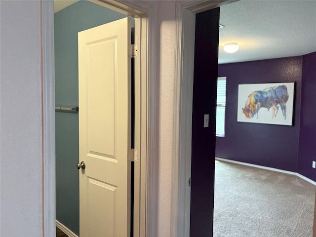 hall featuring a textured ceiling, carpet floors, and baseboards