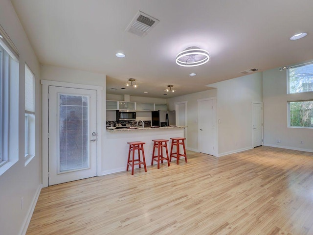 kitchen with appliances with stainless steel finishes, visible vents, a peninsula, and light wood-style floors