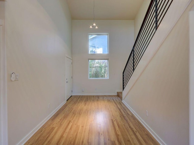 entrance foyer featuring light wood-style floors, baseboards, a high ceiling, and stairs