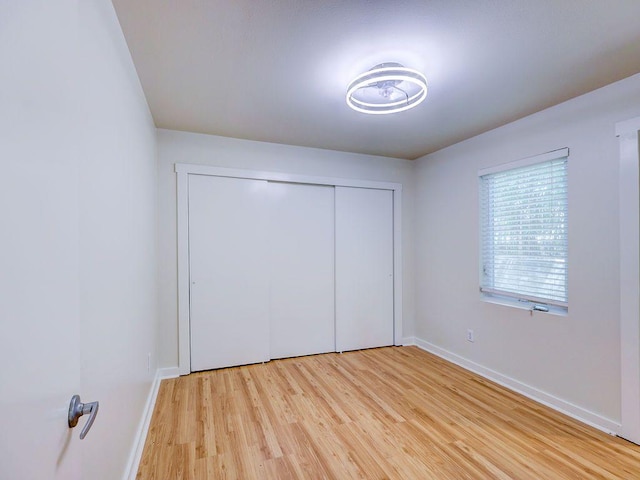 unfurnished bedroom featuring light wood-type flooring, a closet, and baseboards
