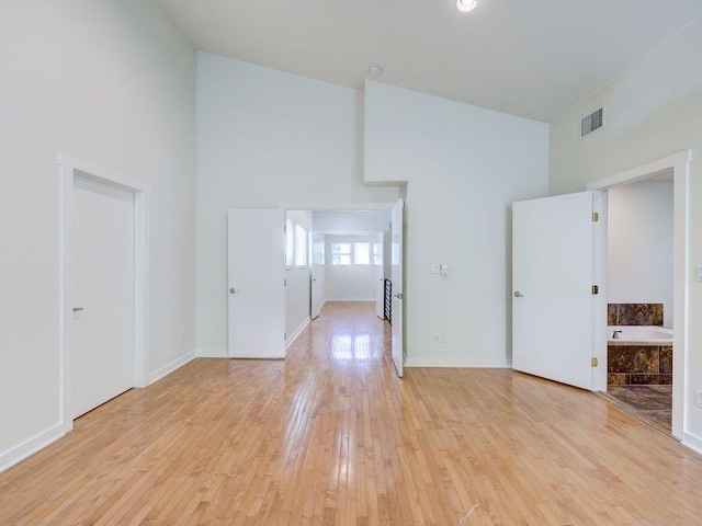 spare room featuring visible vents, baseboards, light wood-style flooring, and a high ceiling