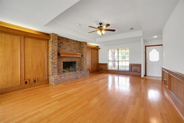 unfurnished living room featuring wainscoting, a raised ceiling, ceiling fan, and light wood-style flooring