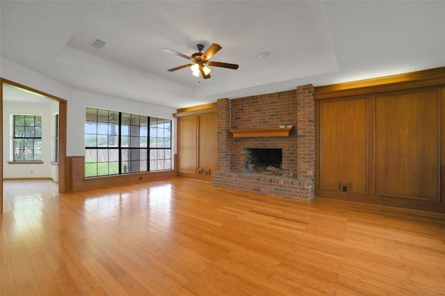 unfurnished living room featuring light wood finished floors, a fireplace, ceiling fan, a tray ceiling, and visible vents