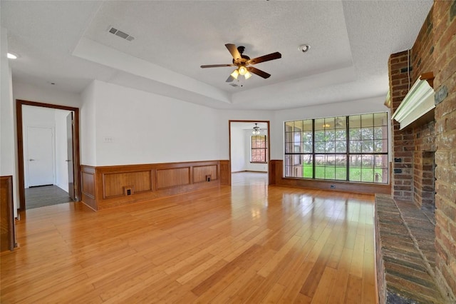 unfurnished living room featuring hardwood / wood-style floors, ceiling fan, a fireplace, visible vents, and a tray ceiling