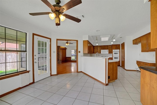 kitchen featuring a ceiling fan, brown cabinets, a peninsula, and white appliances