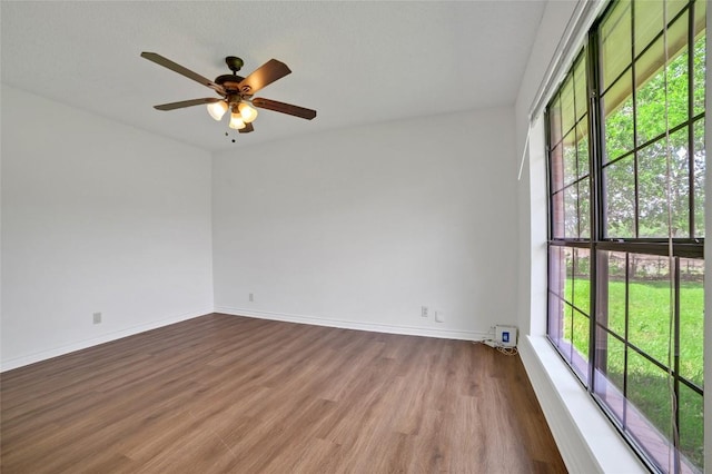 unfurnished room with wood finished floors, ceiling fan, plenty of natural light, and baseboards