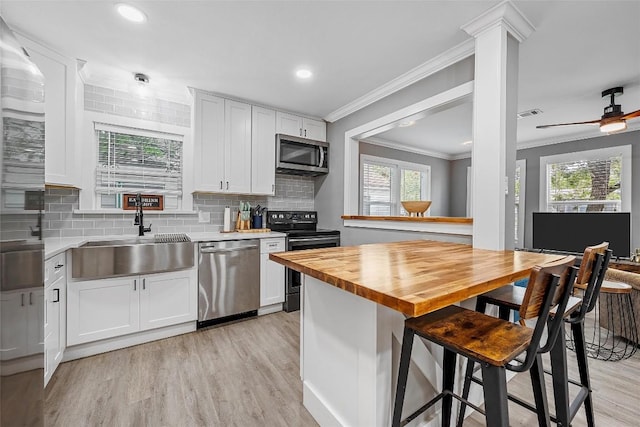 kitchen with a sink, appliances with stainless steel finishes, a healthy amount of sunlight, butcher block countertops, and light wood-type flooring