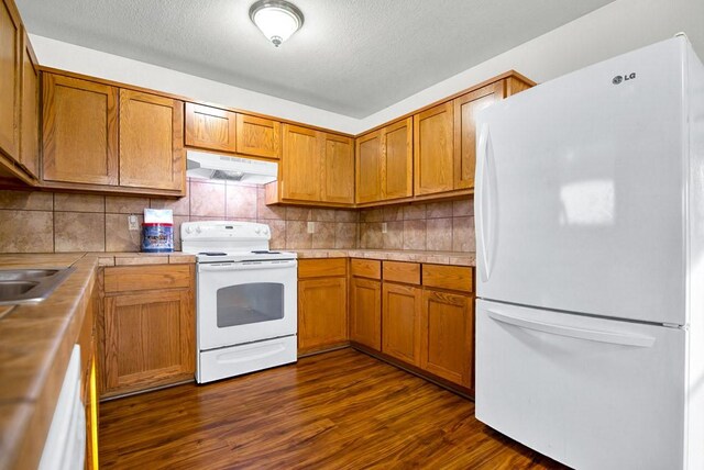 121 Hudson Rd, Smithville, TX 78957 - kitchen featuring white appliances, under cabinet range hood, dark wood finished floors, brown cabinetry, and a textured ceiling