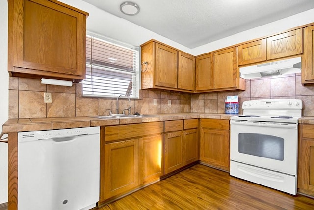 kitchen with white appliances, tile counters, under cabinet range hood, backsplash, and a sink