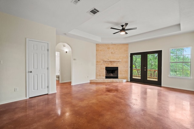 unfurnished living room with arched walkways, concrete floors, ceiling fan, visible vents, and a raised ceiling