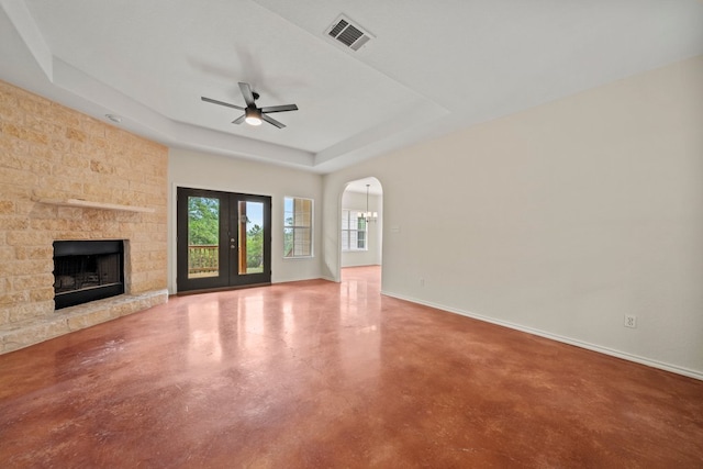 unfurnished living room with finished concrete flooring, visible vents, a tray ceiling, a ceiling fan, and a stone fireplace