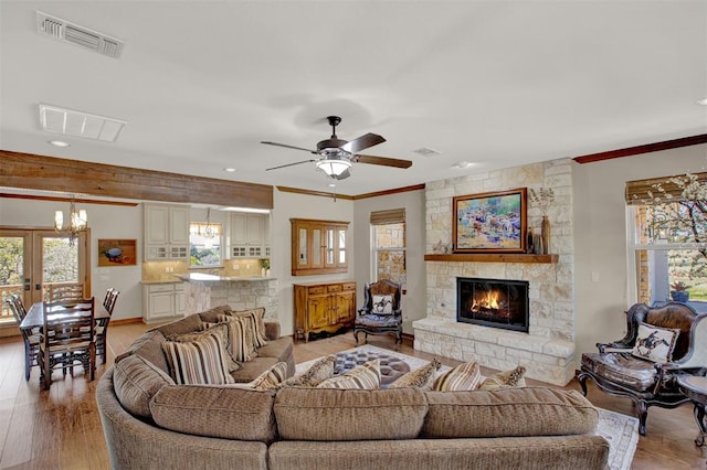 living area featuring a wealth of natural light, visible vents, crown molding, and a stone fireplace