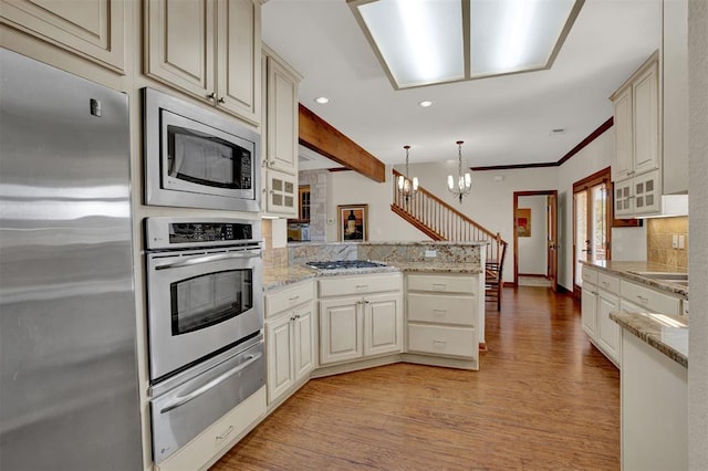 kitchen featuring an inviting chandelier, a warming drawer, light wood-style flooring, a peninsula, and appliances with stainless steel finishes