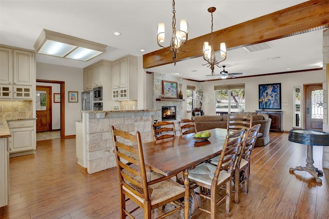 dining room featuring hardwood / wood-style flooring, baseboards, a stone fireplace, and ceiling fan with notable chandelier