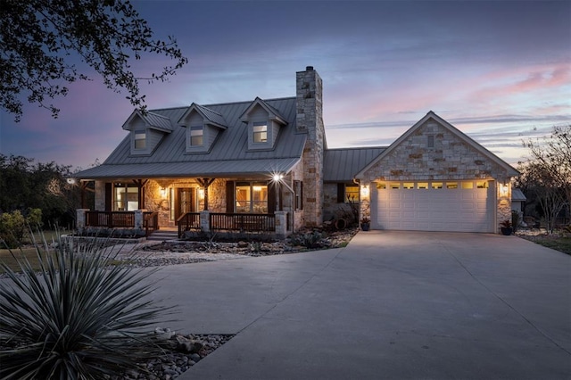 cape cod home with driveway, a chimney, an attached garage, and stone siding