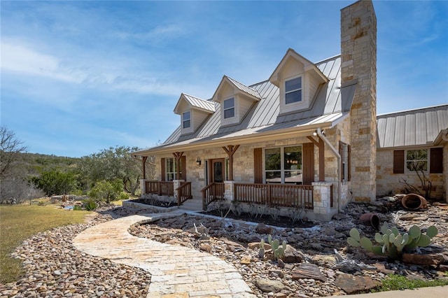 view of front of home featuring stone siding, a chimney, metal roof, a standing seam roof, and a porch