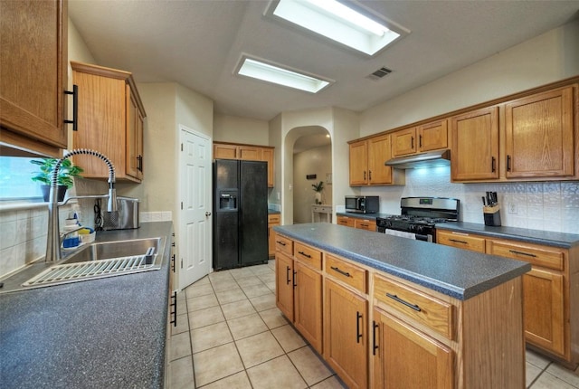 kitchen featuring a sink, stainless steel appliances, under cabinet range hood, a kitchen island, and arched walkways