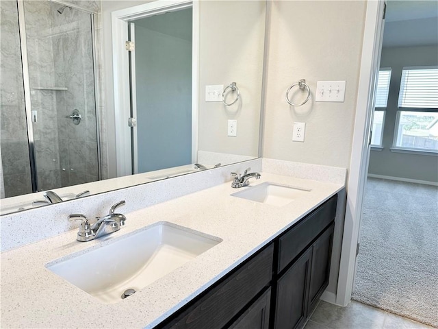 full bath with baseboards, a shower stall, double vanity, and a sink