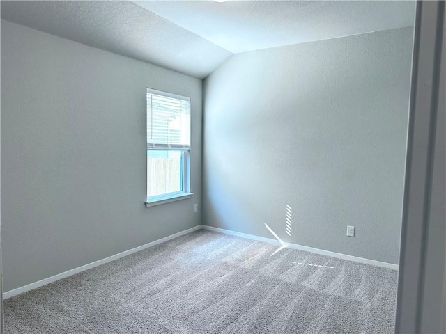 carpeted spare room with a textured wall, lofted ceiling, and baseboards