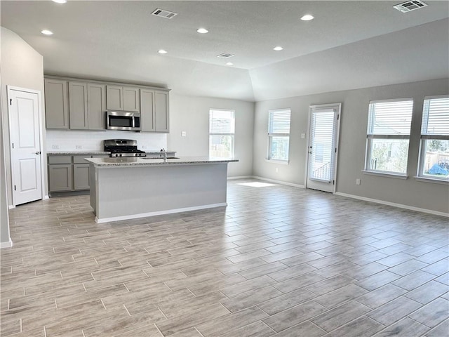 kitchen with stainless steel appliances, a sink, gray cabinetry, visible vents, and open floor plan