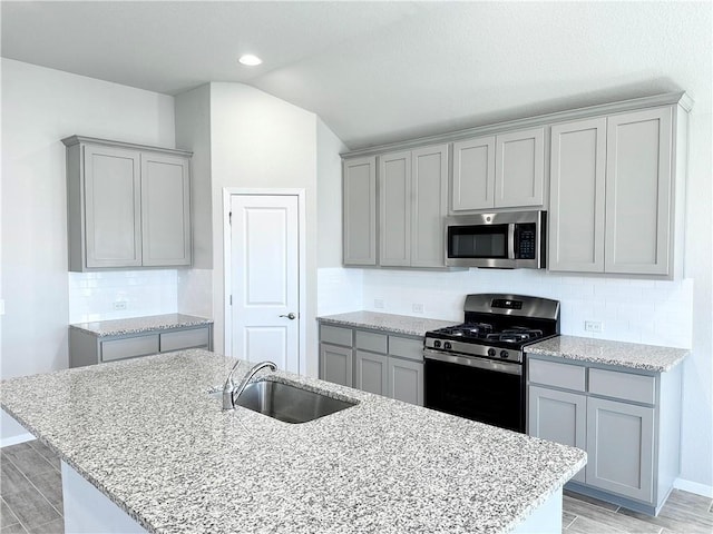 kitchen featuring gray cabinets, light wood-style flooring, stainless steel appliances, a sink, and lofted ceiling