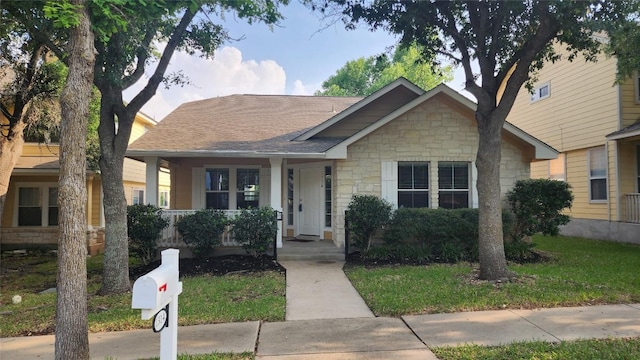 bungalow-style home featuring a front yard, covered porch, stone siding, and a shingled roof