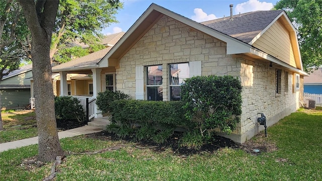 view of side of property with a lawn, stone siding, central AC, and a shingled roof