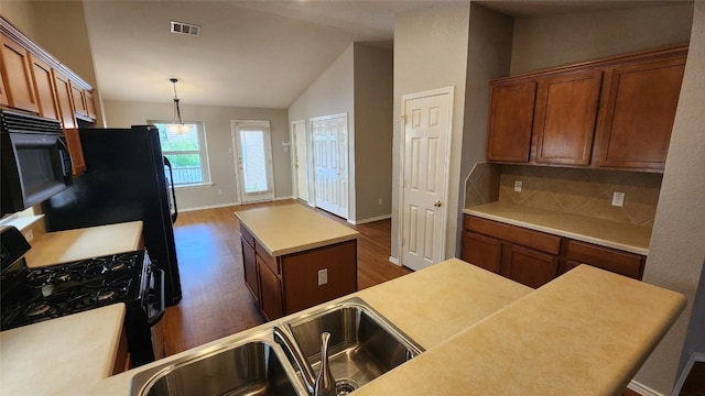 kitchen featuring lofted ceiling, a center island, black appliances, dark wood finished floors, and brown cabinetry